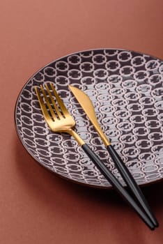 Empty ceramic plate on a monochrome brown background. Empty plate with cutlery on a dining table