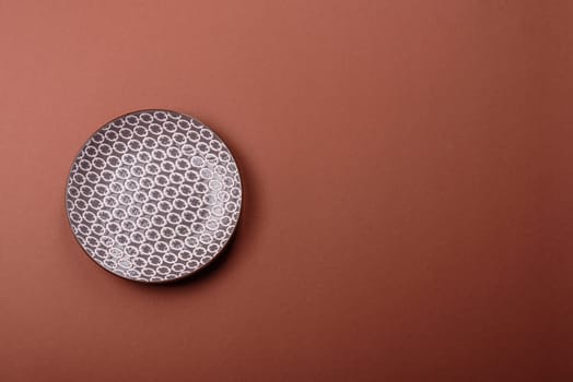 Empty ceramic plate on a monochrome brown background. Empty plate with cutlery on a dining table
