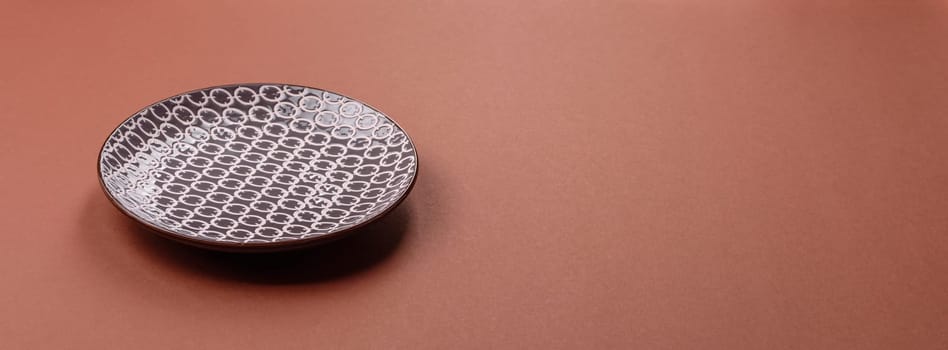 Empty ceramic plate on a monochrome brown background. Empty plate with cutlery on a dining table