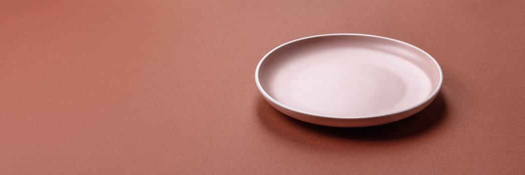 Empty ceramic plate on a monochrome brown background. Empty plate with cutlery on a dining table