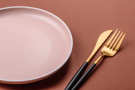 Empty ceramic plate on a monochrome brown background. Empty plate with cutlery on a dining table