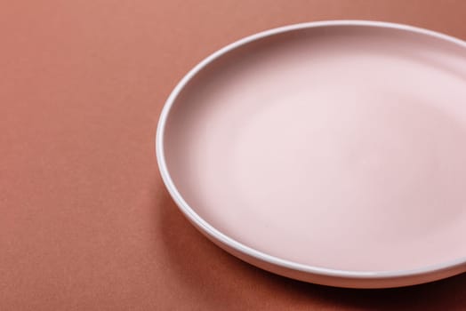 Empty ceramic plate on a monochrome brown background. Empty plate with cutlery on a dining table