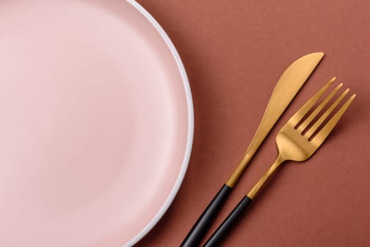 Empty ceramic plate on a monochrome brown background. Empty plate with cutlery on a dining table