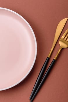 Empty ceramic plate on a monochrome brown background. Empty plate with cutlery on a dining table
