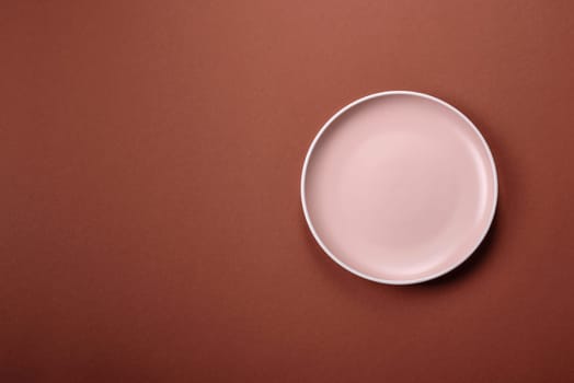Empty ceramic plate on a monochrome brown background. Empty plate with cutlery on a dining table