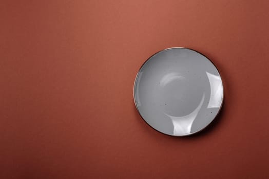 Empty ceramic plate on a monochrome brown background. Empty plate with cutlery on a dining table