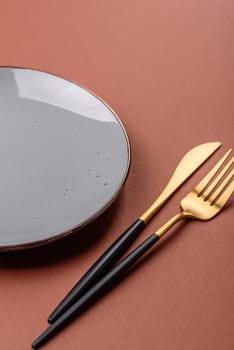 Empty ceramic plate on a monochrome brown background. Empty plate with cutlery on a dining table