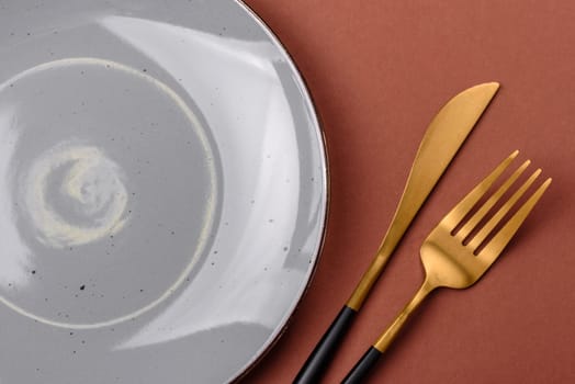 Empty ceramic plate on a monochrome brown background. Empty plate with cutlery on a dining table