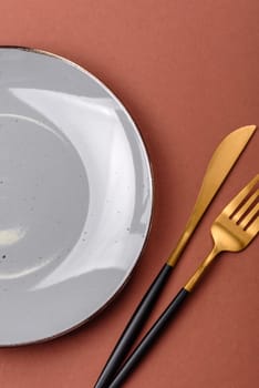 Empty ceramic plate on a monochrome brown background. Empty plate with cutlery on a dining table