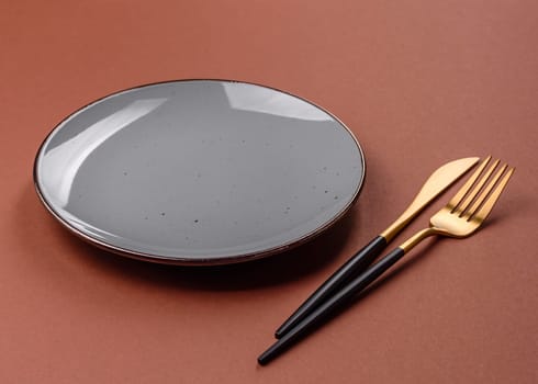 Empty ceramic plate on a monochrome brown background. Empty plate with cutlery on a dining table