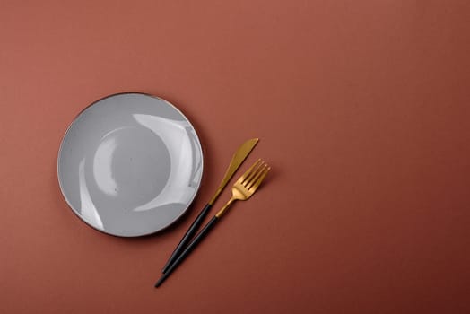 Empty ceramic plate on a monochrome brown background. Empty plate with cutlery on a dining table