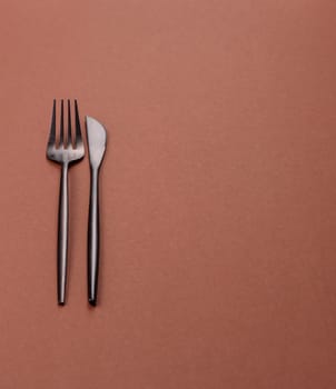 Knife and fork, cutlery on a brown dining table. Utensils and crockery for preparing dinner