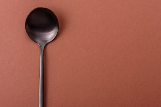 Empty metal spoon on a monochrome brown background. Cutlery on the dining table