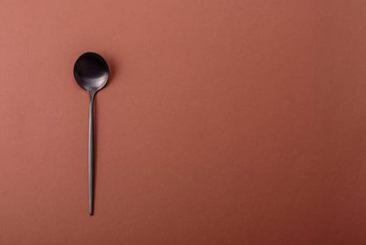Empty metal spoon on a monochrome brown background. Cutlery on the dining table