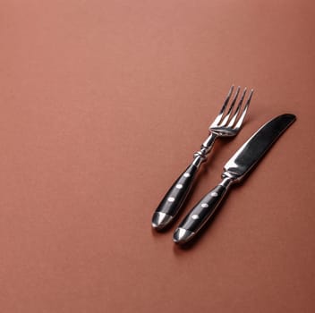 Knife and fork, cutlery on a brown dining table. Utensils and crockery for preparing dinner