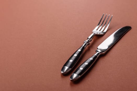 Knife and fork, cutlery on a brown dining table. Utensils and crockery for preparing dinner