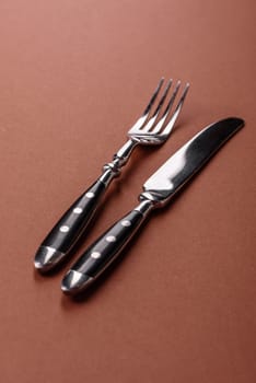 Knife and fork, cutlery on a brown dining table. Utensils and crockery for preparing dinner