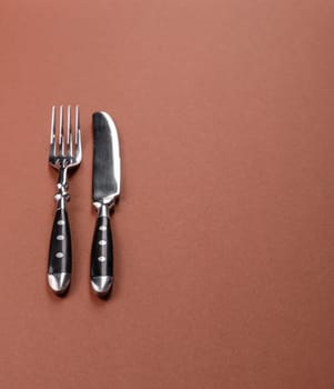 Knife and fork, cutlery on a brown dining table. Utensils and crockery for preparing dinner