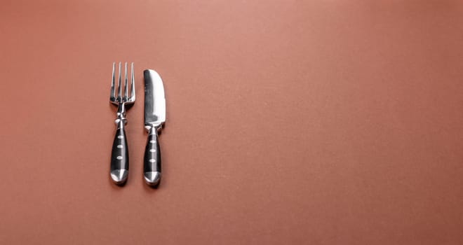 Knife and fork, cutlery on a brown dining table. Utensils and crockery for preparing dinner