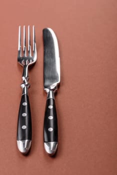 Knife and fork, cutlery on a brown dining table. Utensils and crockery for preparing dinner