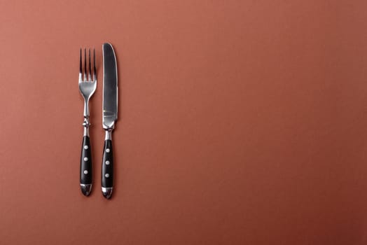 Knife and fork, cutlery on a brown dining table. Utensils and crockery for preparing dinner