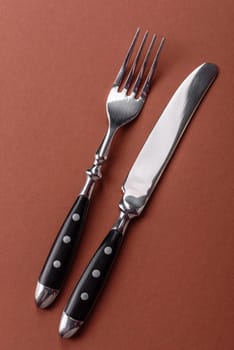 Knife and fork, cutlery on a brown dining table. Utensils and crockery for preparing dinner