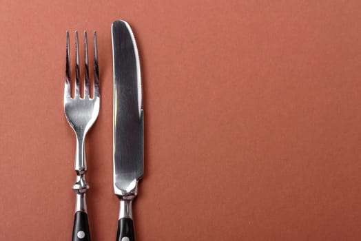 Knife and fork, cutlery on a brown dining table. Utensils and crockery for preparing dinner
