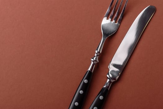 Knife and fork, cutlery on a brown dining table. Utensils and crockery for preparing dinner
