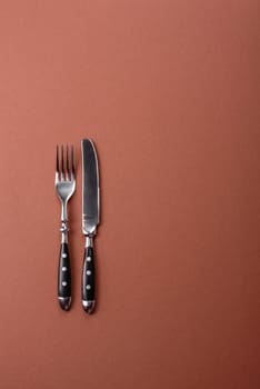 Knife and fork, cutlery on a brown dining table. Utensils and crockery for preparing dinner