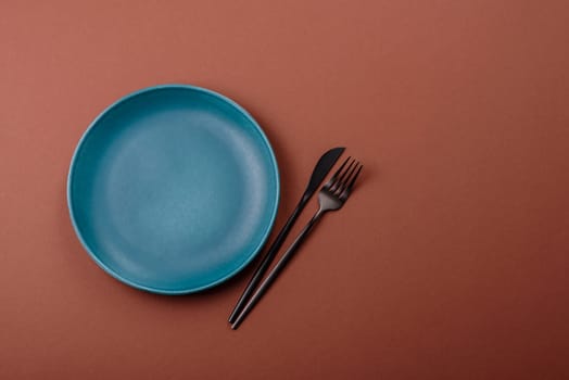 Empty ceramic plate on a monochrome brown background. Empty plate with cutlery on a dining table