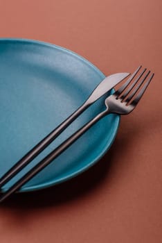 Empty ceramic plate on a monochrome brown background. Empty plate with cutlery on a dining table