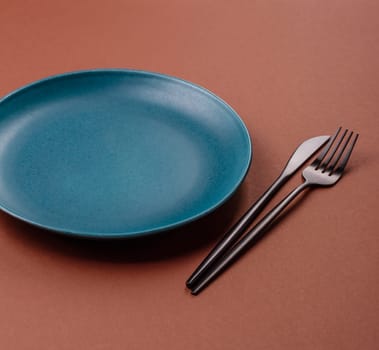 Empty ceramic plate on a monochrome brown background. Empty plate with cutlery on a dining table