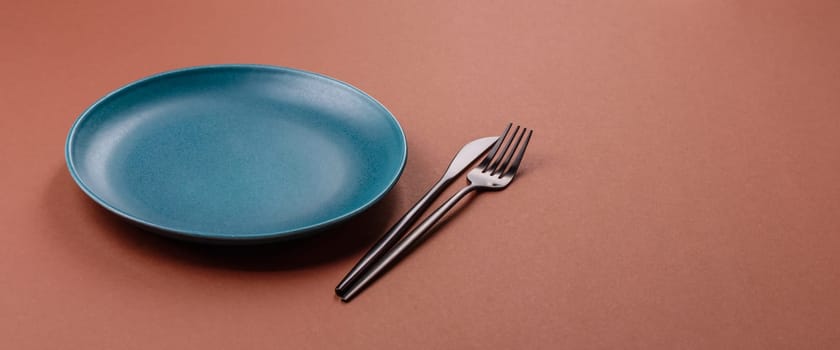 Empty ceramic plate on a monochrome brown background. Empty plate with cutlery on a dining table