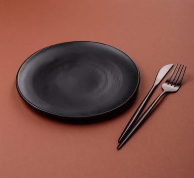 Empty ceramic plate on a monochrome brown background. Empty plate with cutlery on a dining table