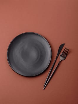 Empty ceramic plate on a monochrome brown background. Empty plate with cutlery on a dining table