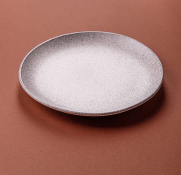 Empty ceramic plate on a monochrome brown background. Empty plate with cutlery on a dining table