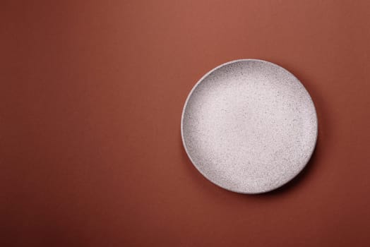 Empty ceramic plate on a monochrome brown background. Empty plate with cutlery on a dining table