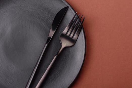 Empty ceramic plate on a monochrome brown background. Empty plate with cutlery on a dining table