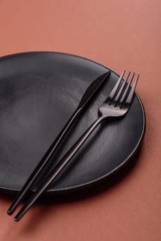 Empty ceramic plate on a monochrome brown background. Empty plate with cutlery on a dining table