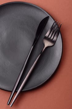 Empty ceramic plate on a monochrome brown background. Empty plate with cutlery on a dining table