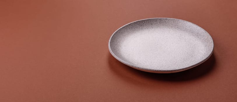 Empty ceramic plate on a monochrome brown background. Empty plate with cutlery on a dining table
