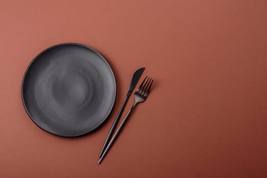 Empty ceramic plate on a monochrome brown background. Empty plate with cutlery on a dining table