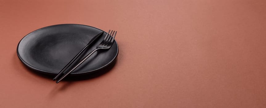 Empty ceramic plate on a monochrome brown background. Empty plate with cutlery on a dining table