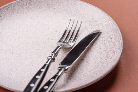 Empty ceramic plate on a monochrome brown background. Empty plate with cutlery on a dining table