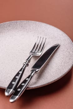 Empty ceramic plate on a monochrome brown background. Empty plate with cutlery on a dining table