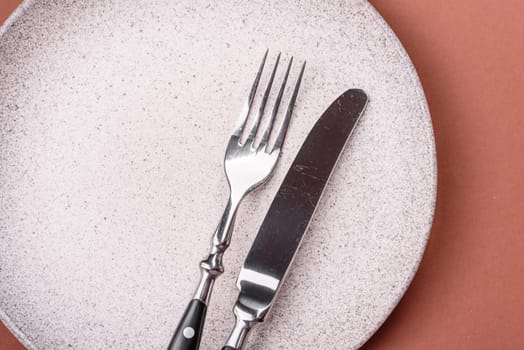 Empty ceramic plate on a monochrome brown background. Empty plate with cutlery on a dining table
