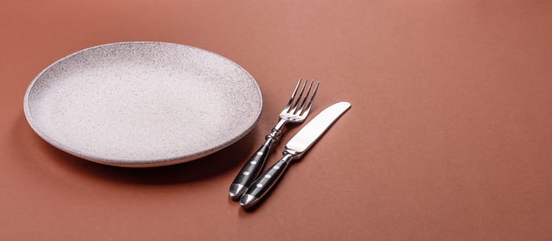Empty ceramic plate on a monochrome brown background. Empty plate with cutlery on a dining table