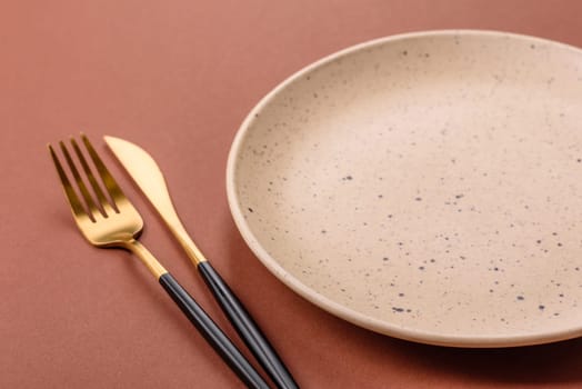 Empty ceramic plate on a monochrome brown background. Empty plate with cutlery on a dining table