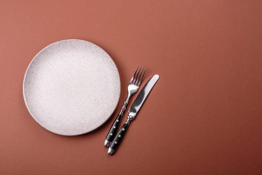 Empty ceramic plate on a monochrome brown background. Empty plate with cutlery on a dining table