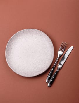 Empty ceramic plate on a monochrome brown background. Empty plate with cutlery on a dining table